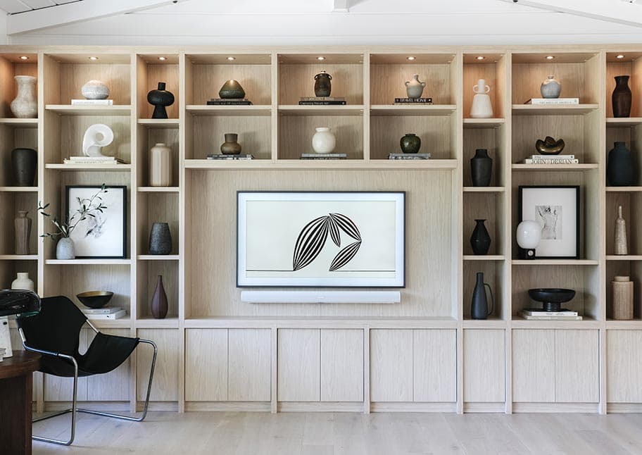 Custom entertainment center in a classic white wood finish with bookshelves, and benches created by California Closets