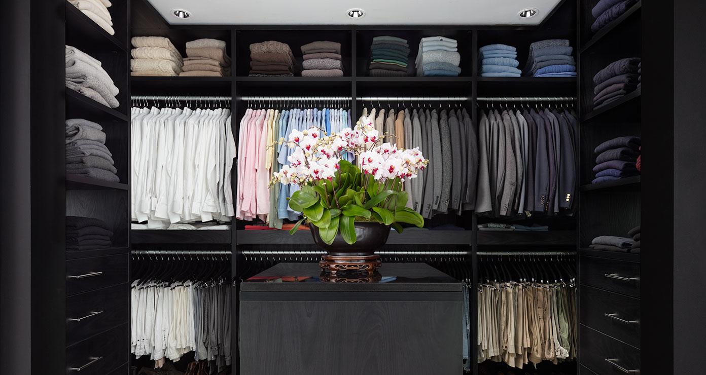 Dark wood finish walk in layout with custom shelving and wardrobe hanging space by California Closets