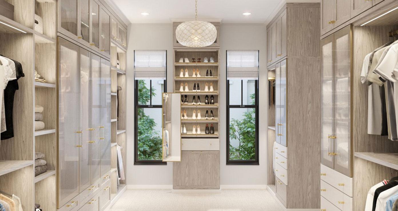 Light finish woman's wardrobe walk in closet designed with glass door cabinets and shoe storage by California Closets